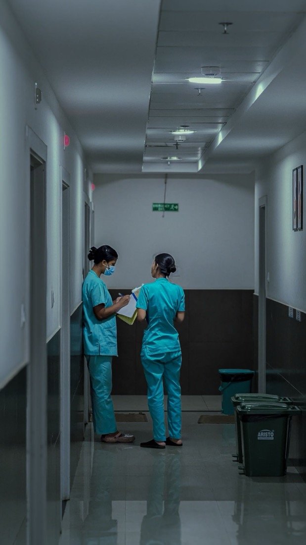 Due operatrici sanitarie in divisa parlano in un corridoio di una struttura